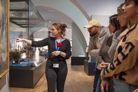 Médiatrice culturelle du musée national de la Marine guidant un groupe de visiteurs devant une peinture maritime, dans une salle d’exposition.
