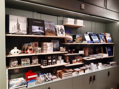 Étagères de la boutique du musée de la Marine de Brest avec des livres sur la Marine et les sous-marins, ainsi que des objets souvenirs et mugs.