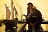 Un enfant dans les bras de son père pointe du doigt une maquette de navire exposée au musée de la Marine à Port-Louis.