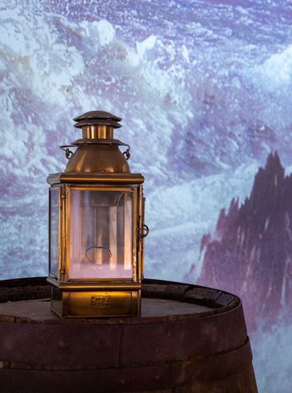 Lanterne en laiton posée sur un tonneau, éclairée devant une projection de vagues déchaînées – musée national de la Marine, Port-Louis.