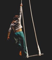 Acrobate suspendue à une corde, en équilibre sur une planche, évoluant dans un espace sombre ; cette performance est proposée par une artiste de l’École nationale des arts du cirque de Rosny.