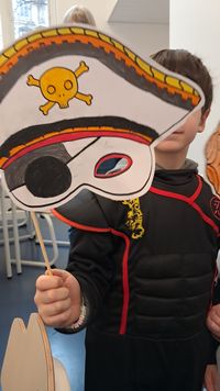 Enfant participant à un atelier, tenant un masque de pirate en carton décoré d’un crâne et d’un cache-œil, dans un espace pédagogique.