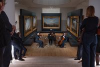 Concert de musique de chambre au cœur des collections du musée national de la Marine, avec un trio à cordes entouré de tableaux maritimes, observé par le public.