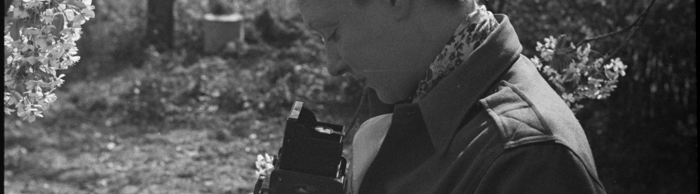 Portrait de Germaine Kanova, photographe du Service cinématographique de l’armée française (SCA), équipée d’un appareil Rolleiflex, debout en extérieur en Bade-Würtemberg (Allemagne), 11 avril 1945. 