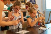 Premier plan avec deux petites filles faisant des noeuds accompagnée d'une adulte