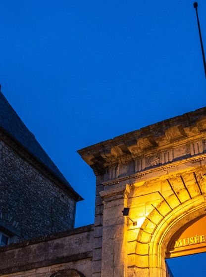 Façade illuminée du musée national de la Marine à Rochefort à la tombée de la nuit, avec son portail d'entrée en pierre.