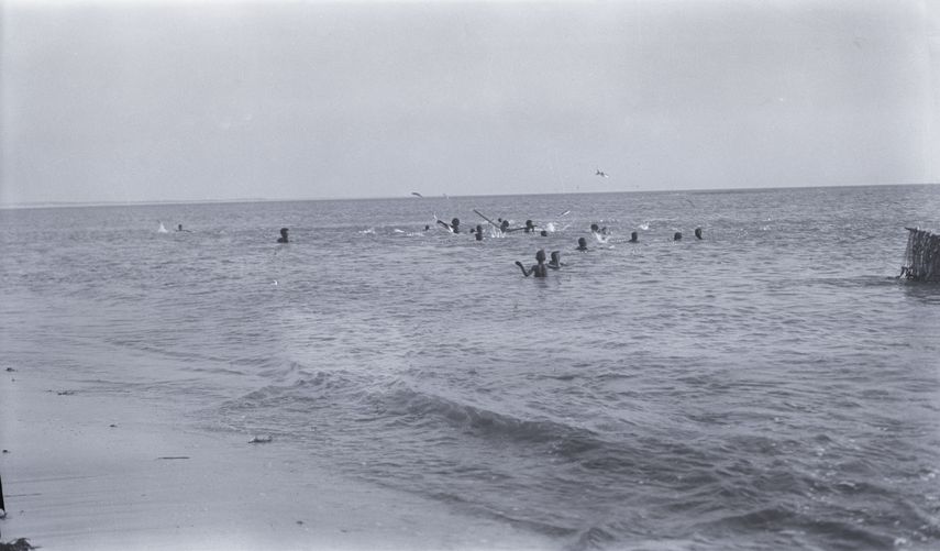 Groupe de jeunes nageant en mer près du rivage, photographiés en noir et blanc ; il s'agit de pêcheurs Imraguens pratiquant une technique traditionnelle de pêche en coopération avec les dauphins, sur la côte mauritanienne.
