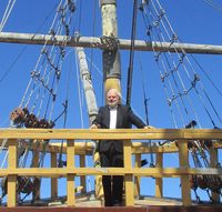 Portrait de Michel Chandeigne à bord de la réplique du navire Victoria, en costume sombre sur le pont.