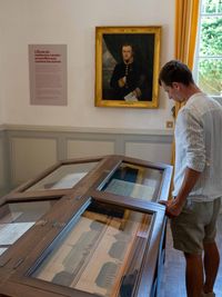 Jeune adulte observant des documents d’archives dans la salle des actes de l’Ancienne École de médecine navale, sous le portrait du médecin naval Laurencin.