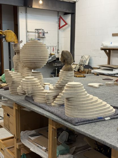 Ensemble de sculptures en bois stratifié installées sur une table d’atelier, représentant des formes évoquant des paysages ou des volumes marins.