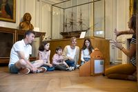 Famille avec trois enfant d'âges différent écoutant une médiatrice assis par terre