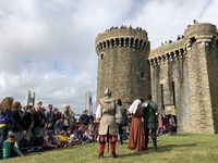Des personnages costumés font face à un public attentif devant les remparts du château