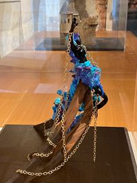 Sculpture contemporaine représentant une figure féminine noire enchaînée par une chaine dorée, entourée de résine bleue et violette, exposée dans une vitrine du musée.