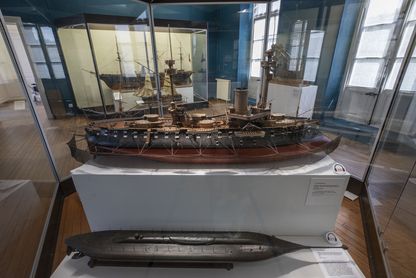Salle des cuirassés au musée national de la Marine à Rochefort, illustrant les évolutions de la Marine au 19e siècle, avec au premier plan une maquette de cuirassé sur socle blanc et une maquette de sous-marin