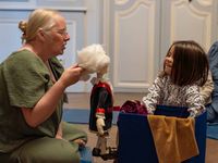 Adulte animant une activité avec un bébé assis, autour d’objets colorés et de marionnettes dans une salle du musée